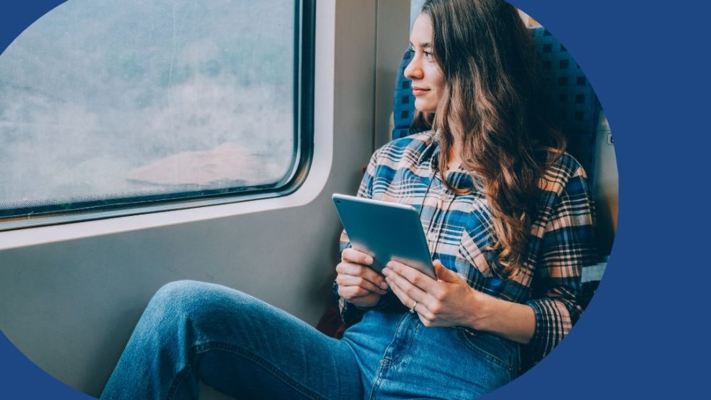 A traveller looking out a window on a train using technology to check a change to her itinerary.