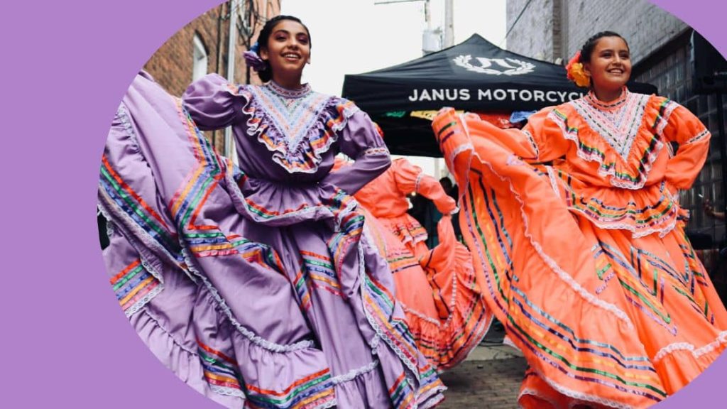 Two cultural dances smiling as they swish their traditional dresses. 