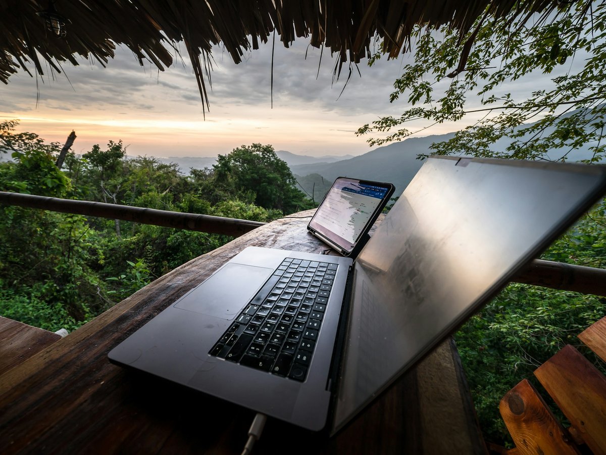 How much does travel software cost feature image Laptop and phone on a wooden lodge table overlooking forested mountains at sunrise, a travel designer's remote workspace